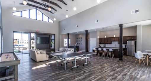 A spacious living room with a pool table and a kitchen area in the background.
