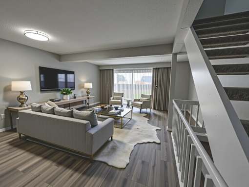 A living room with a grey couch, a white rug, and a staircase.
