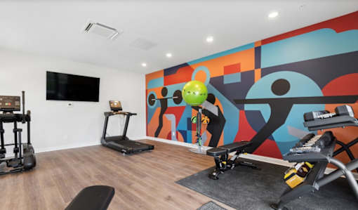 A room with a treadmill, a stationary bike, a weight bench and a television.