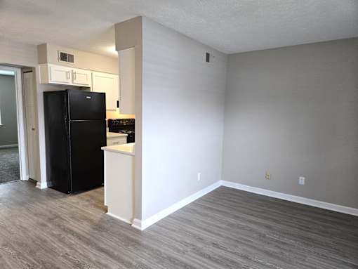 A black refrigerator is in a kitchen with a white wall and a wooden floor.