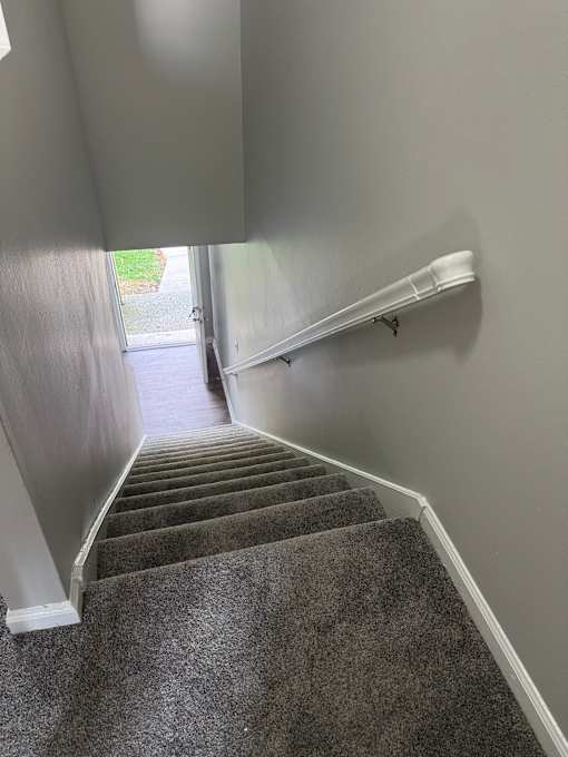 A staircase with a grey carpeted runner and white handrails.