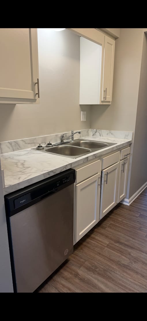 A kitchen with a stainless steel dishwasher and white cabinets.