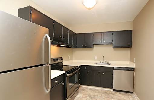 A kitchen with black cabinets and a stainless steel refrigerator.