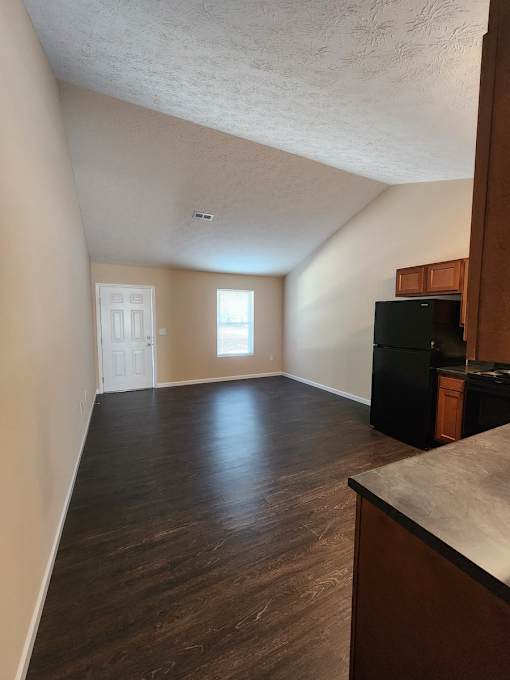 A room with a black fridge and wooden floors.