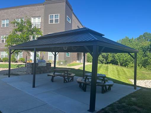 A covered picnic area with benches is situated in front of a building.