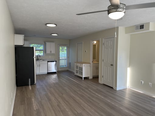 an empty living room and kitchen with wood floors and a black refrigerator