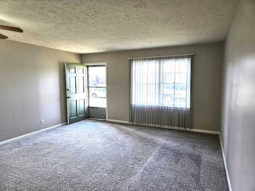 A room with a carpeted floor and a window with blinds.