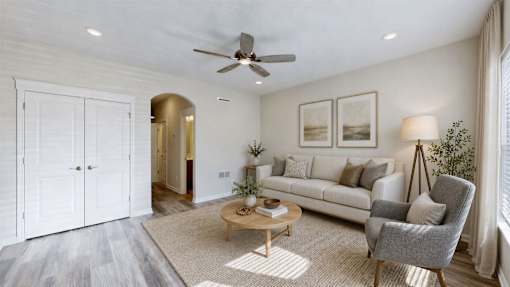 A living room with a white couch, a grey armchair, a wooden coffee table, and a ceiling fan.