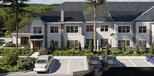 A large, two-story house with a grey roof and white walls is surrounded by a parking lot with several cars.