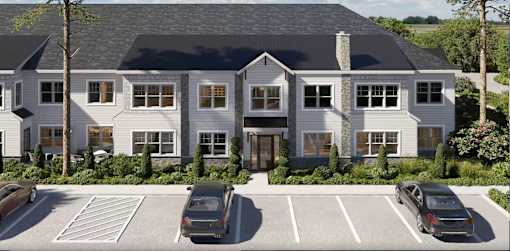 A large white house with a black roof and a parking lot in front.