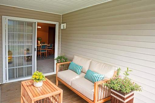 A white couch with blue pillows sits on a wooden deck.