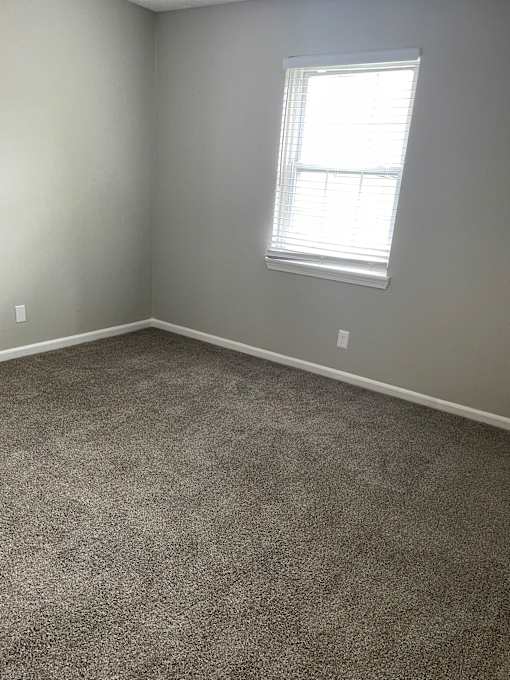 A room with a carpeted floor and a window with blinds.