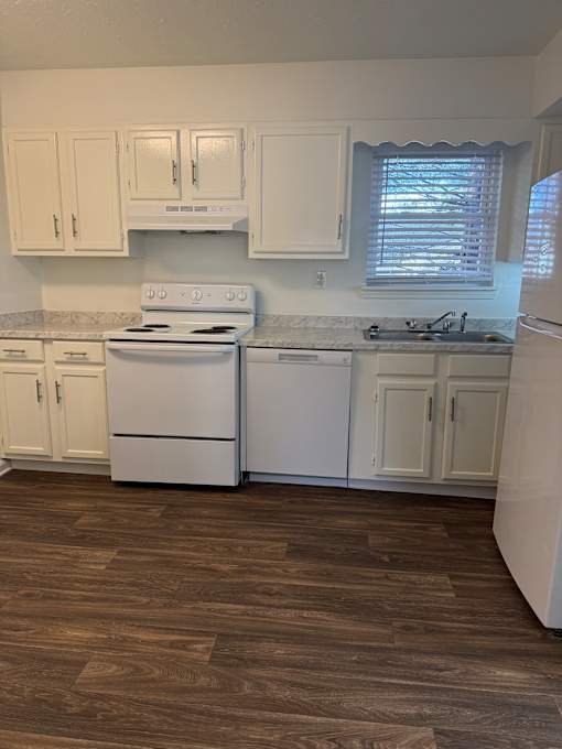 A kitchen with white appliances and wooden floors.