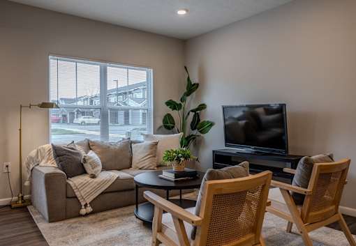 A living room with a grey couch, a television, and two wooden chairs.