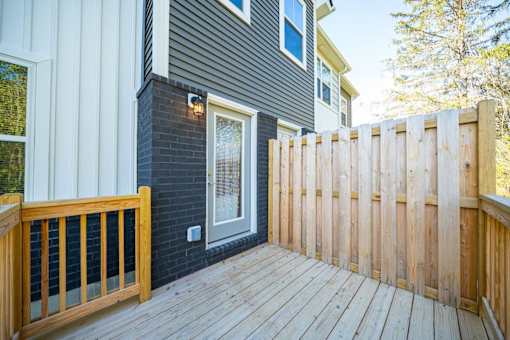 A wooden deck leads to a house with a grey siding and a white window.