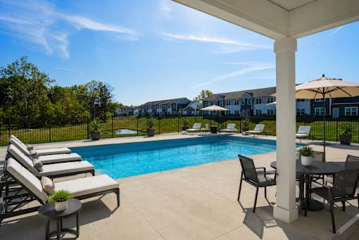 A pool surrounded by lounge chairs and a table under a white pergola.