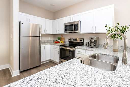 A kitchen with a refrigerator, microwave, oven, and sink.