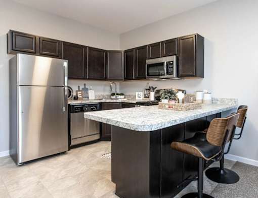 A kitchen with a marble countertop and a stainless steel refrigerator.