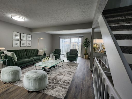 A living room with a green couch, a glass coffee table, and a staircase.