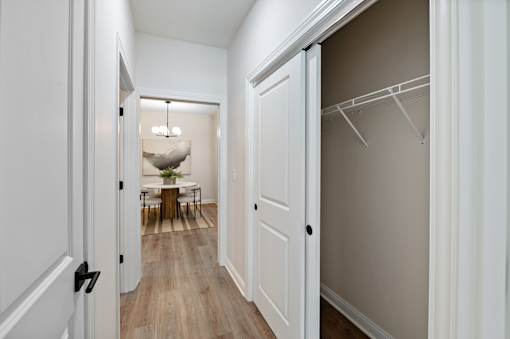 A hallway with a white door on the left and a white closet with a hanger on the right.