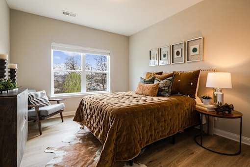 A bedroom with a bed, a chair, a table with a lamp and a potted plant.