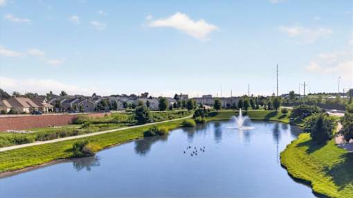 A serene park with a pond, a fountain, and a clear blue sky.