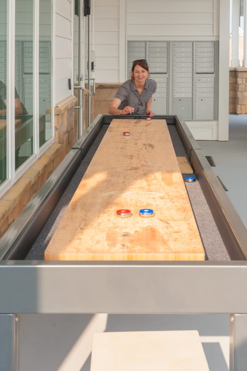 a woman plays a game of shuffleboard on a large shuffleboard table  at The Edison at Madison, Alabama