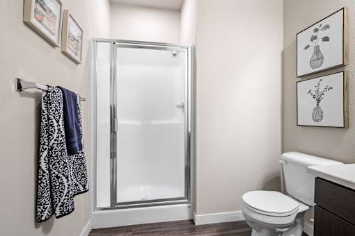 A bathroom with a toilet, a shower with a glass door, and towels hanging on a rack.