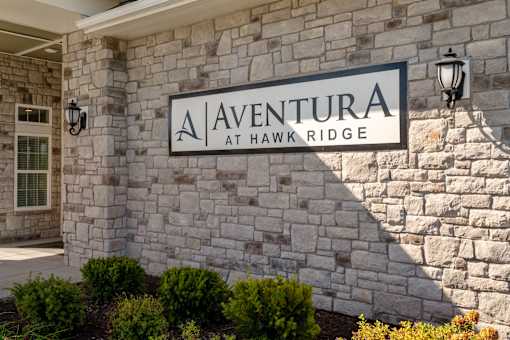 A sign that says "Aventura at Hawk Ridge" is mounted on a stone wall.
