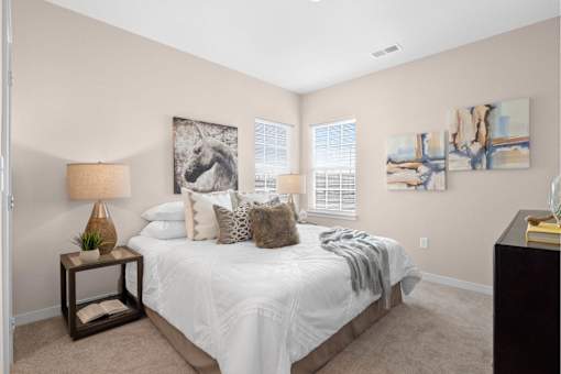 A bedroom with a large bed, a lamp, and two paintings on the wall at Aventura at Wentzville I & II Apartments, Wentzville, MO, 63385