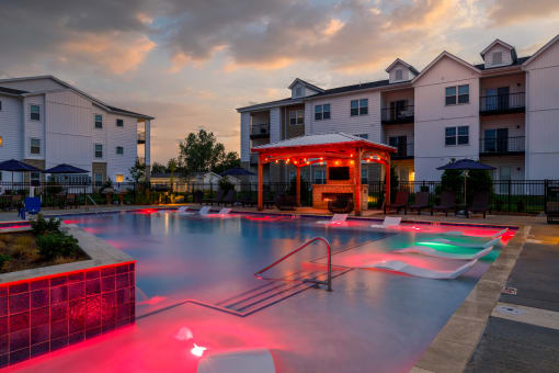 an apartment complex with an outdoor pool and gazebo at dusk  at The Edison at Tiffany Springs, Missouri, 64153