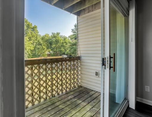 a door opens to a balcony with a view of trees and a blue sky