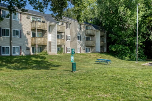 a grassy area with a picnic table in front of an apartment building