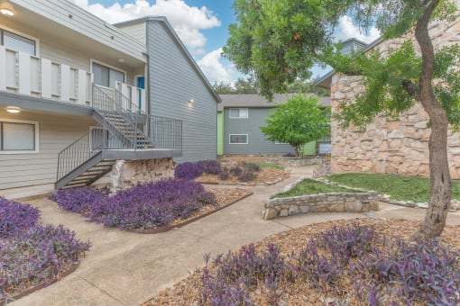 a patio with a stone wall and purple flowers in front of a building at The Escapade, San Antonio, Texas