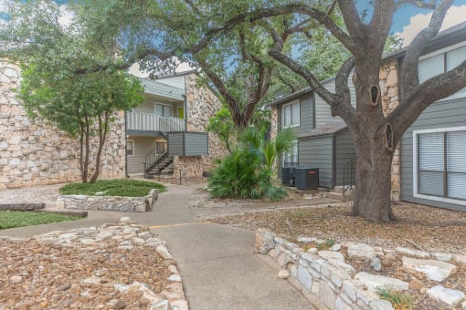 a walkway between two buildings with trees and rocks at The Escapade, San Antonio