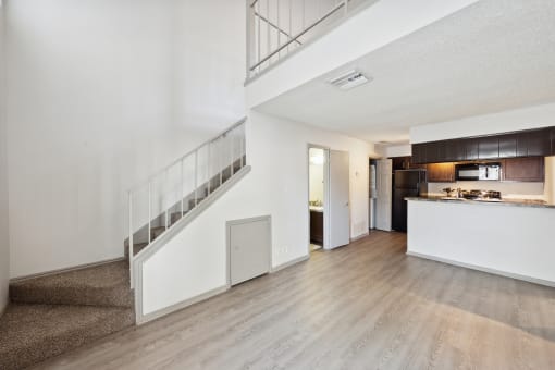 the living room and kitchen of an apartment with white walls and wood floors