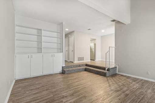 a living room with white walls and wood flooring and a staircase at The Escapade, San Antonio, 78216