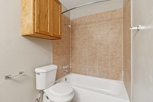 A bathroom with a toilet, tub, and wooden cabinet at Knoll Crest, San Antonio, Texas 78240