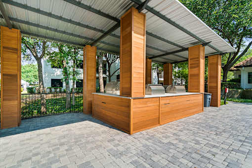 A wooden structure with a roof and pillars is situated on a brick path.