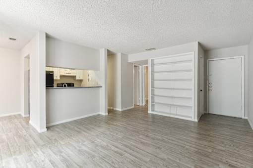 the living room and kitchen of a renovated apartment with white walls and wood floors at The Escapade, San Antonio, TX