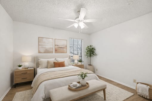 A bedroom with a bed, nightstand, and a plant.