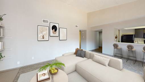 A living room with a white couch, a coffee table with a book and a plant on it, and a wall with three framed pictures.