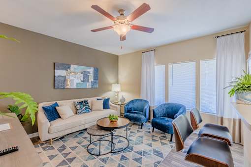 A living room with a white couch, blue chairs, a coffee table, and a ceiling fan.