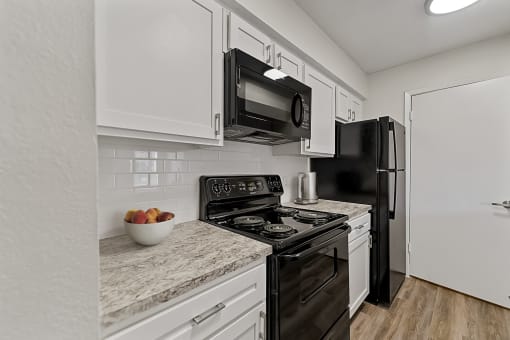a kitchen with white cabinets and black appliances at The Hudson, Texas