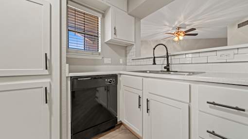 an empty kitchen with white cabinets and a black dishwasher at Polo Clubs Apartments, Austin, TX