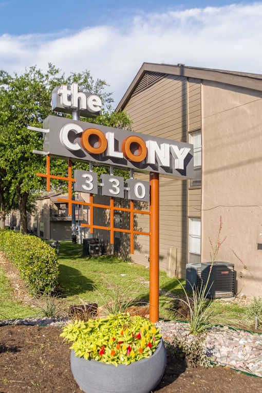 Monument sign with modern orange framework and flower bed at The Colony Apartments, Texas