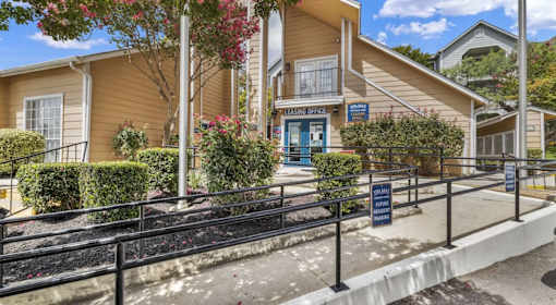 A building with a blue sign that says "Parking Office" is surrounded by bushes and trees.