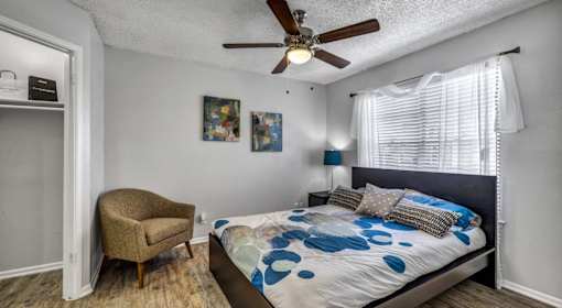 A bedroom with a bed, chair, and ceiling fan.
