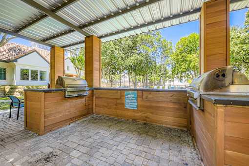 A wooden kiosk with a metal roof is situated on a paved area with a blue sign on it.