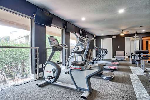 A gym with a row of treadmills and elliptical machines.